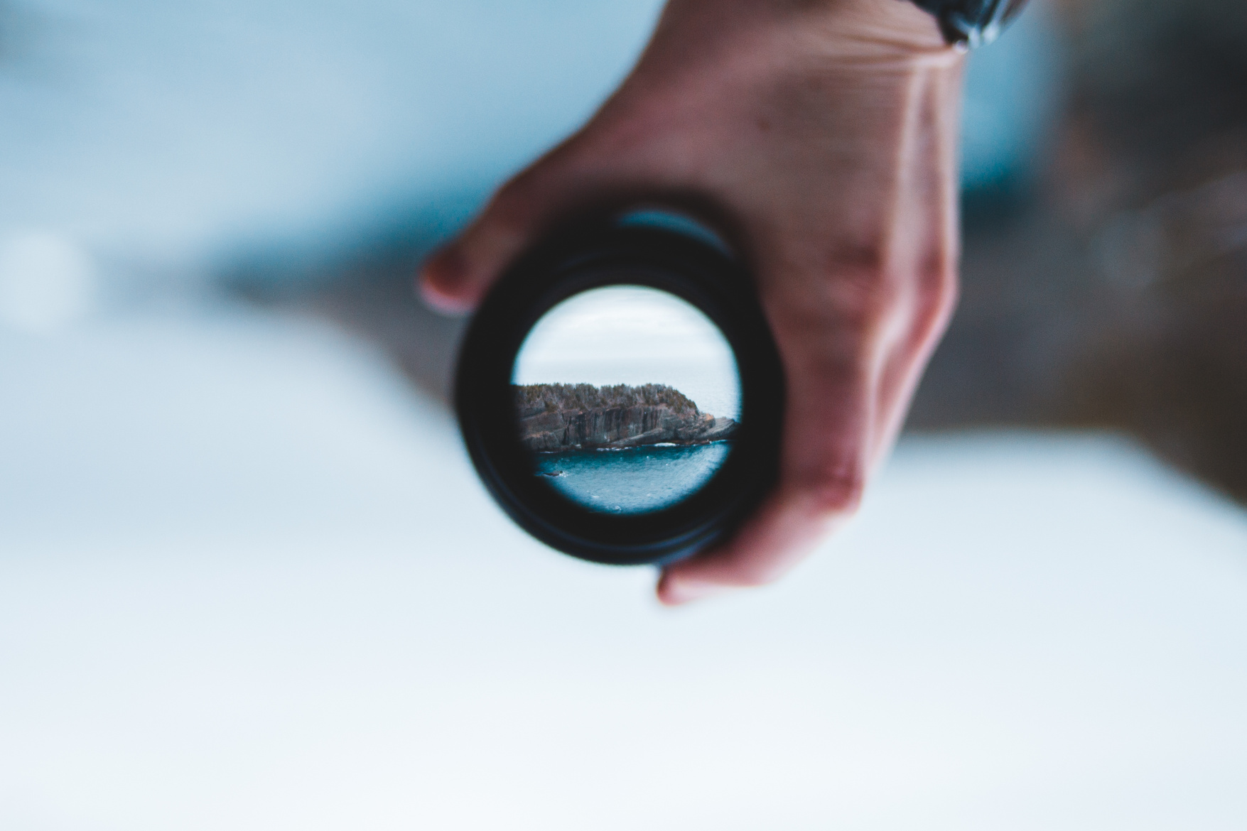 Crop man holding camera lens against sea cliff